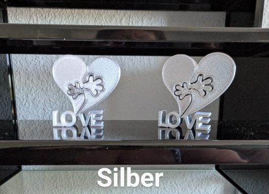 Zwei silberne Dekoherzen mit der Aufschrift „LOVE“ auf einem Regal.