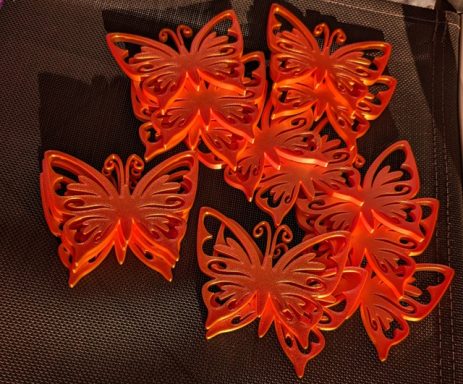 Sieben orangefarbene Schmetterlingsornamente auf einem dunklen Hintergrund.