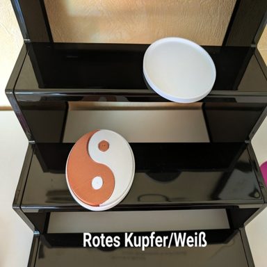 Zwei Schalen auf einem schwarzen Regal, eine rot-weiße Yin-Yang-Form und eine weiße Schale.