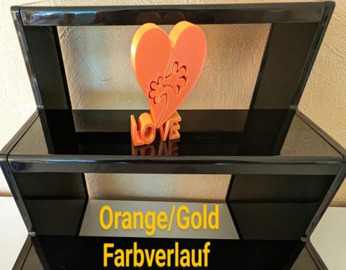 Herz in Orange/Gold auf schwarzem Regal mit beschriftetem Farbhintergrund.