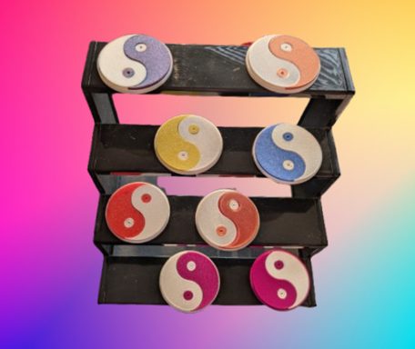 Drei Regale mit runden Yin-Yang-Symbolen in verschiedenen Farben auf einem bunten Hintergrund.