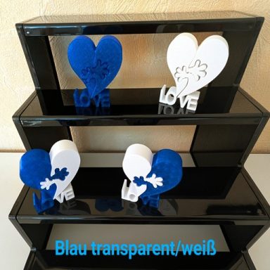 Drei dekorative Herzen in Blau und Weiß, platziert auf einem schwarzen Regal.